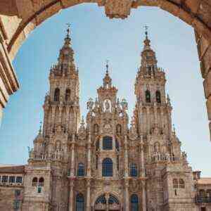 Tomada desde el interior de un arco de piedra que enmarca la imagen, esta fotografía ofrece una perspectiva impactante de la fachada barroca de la catedral de Santiago de Compostela. Sus dos torres ornamentadas se elevan hacia un cielo azul luminoso, mientras los detalles esculpidos de la fachada churrigueresca revelan una extraordinaria riqueza artística. Este punto de vista, desde el pórtico de los peregrinos, simboliza el fin del viaje para todos aquellos que han recorrido la Vía de la Plata a través de España. Esta imagen, captada con maestría, ilustra la recompensa espiritual y cultural que aguarda al final del camino.