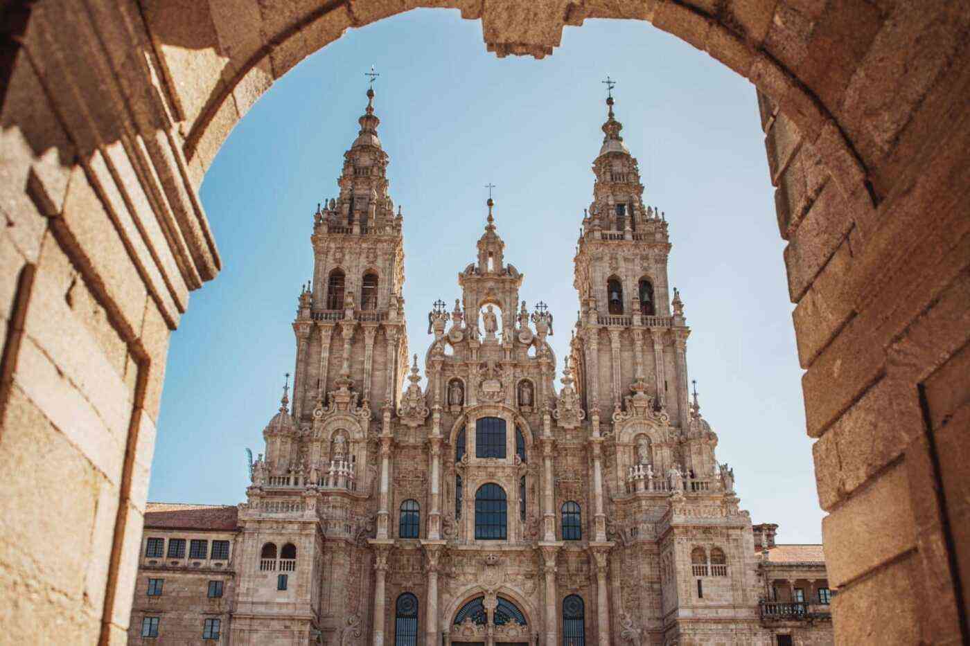 Tomada desde el interior de un arco de piedra que enmarca la imagen, esta fotografía ofrece una perspectiva impactante de la fachada barroca de la catedral de Santiago de Compostela. Sus dos torres ornamentadas se elevan hacia un cielo azul luminoso, mientras los detalles esculpidos de la fachada churrigueresca revelan una extraordinaria riqueza artística. Este punto de vista, desde el pórtico de los peregrinos, simboliza el fin del viaje para todos aquellos que han recorrido la Vía de la Plata a través de España. Esta imagen, captada con maestría, ilustra la recompensa espiritual y cultural que aguarda al final del camino.