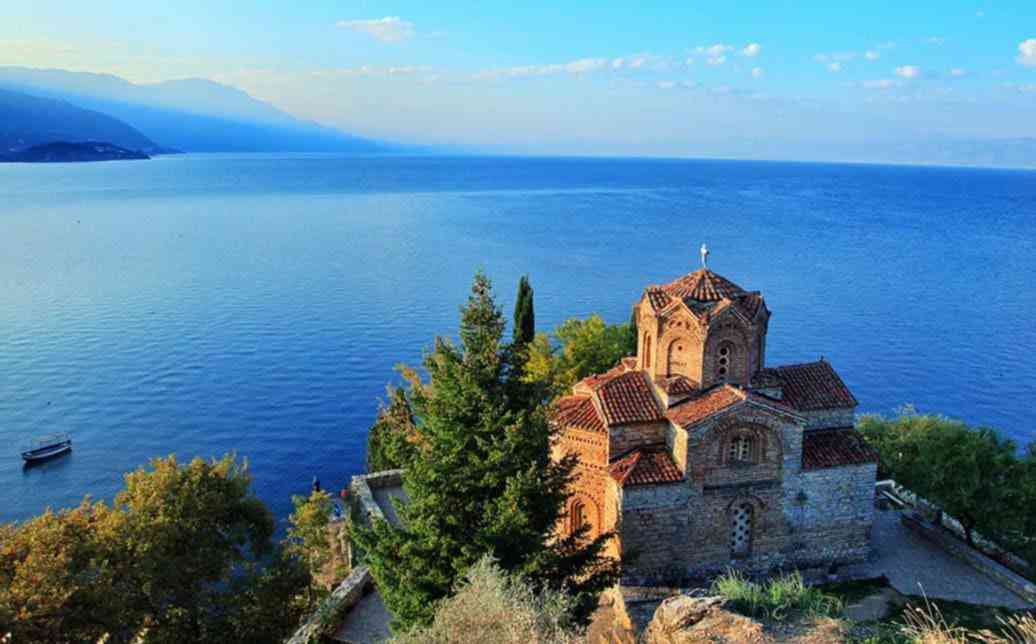 Iglesia de San Juan Kaneo situada sobre un acantilado con vistas al inmenso lago Ohrid bajo un cielo azul.