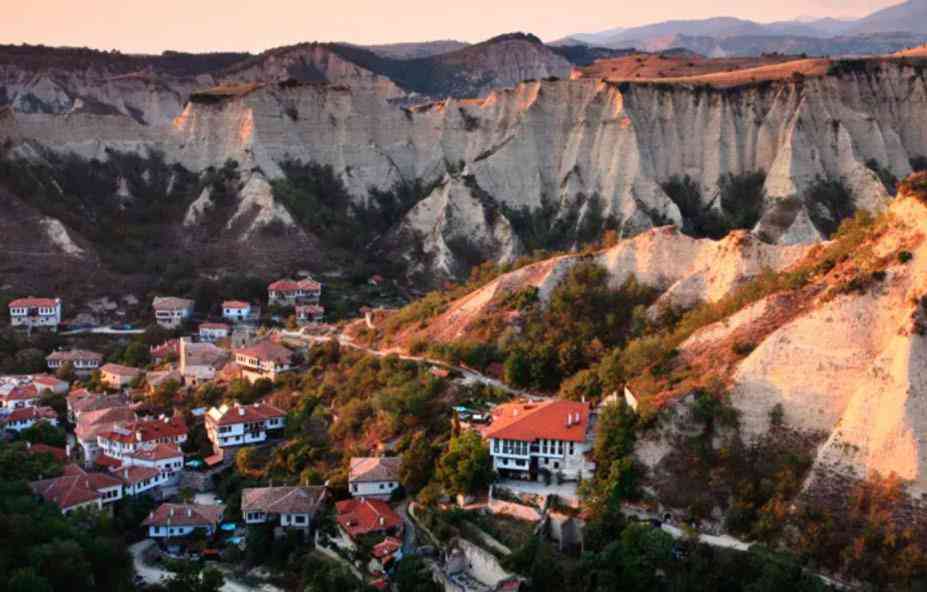 Vista panorámica del histórico pueblo de Melnik rodeado de espectaculares formaciones rocosas y pirámides de arena al atardecer.